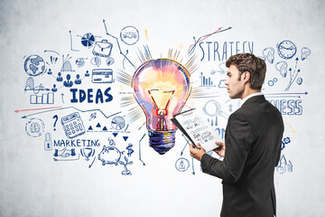 Businessman with clipboard and business sketch with light bulb on concrete wall