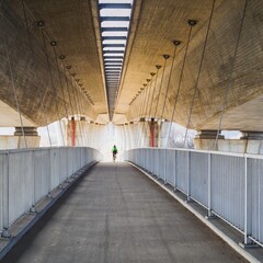 Cyclist in a green jacket and a helmet on his head coming down from a footbridge suspended under a...