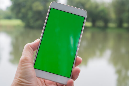 Green blank screen Mock Up phone for advertising. Selfie photo using smartphone for selfies at river landscape park scenery for peaceful in spring when self-isolate from COVID-19 outbreak disease