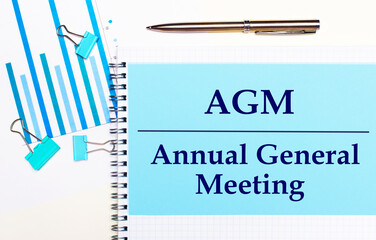 On a light background - light blue diagrams, paper clips and a sheet of paper with the text AGM...