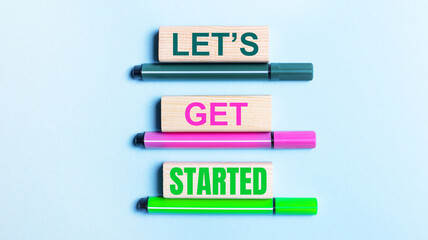 On a light blue background, there are three multi-colored felt-tip pens and wooden blocks with the LET IS GET STARTED text.