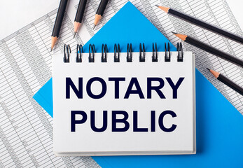 White notebook with the text NOTERY PUBLIC on the table next to black pencils on a blue background...