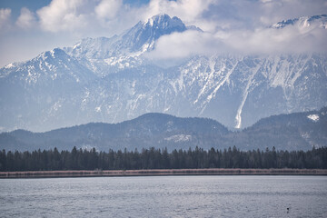 lake and majestic mountains in winter with clouds and fog in the sky