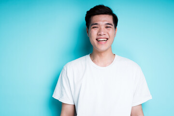 Happy young guy with asian appearance smiling and looking at camera while standing against blue background