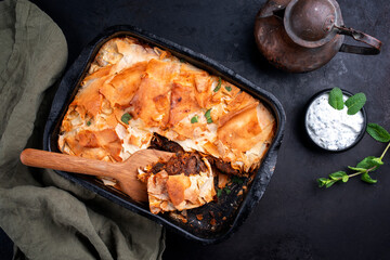 Traditional spiced Moroccan lamb ragout with filo pie served as top view in a rustic black backing dish on a board