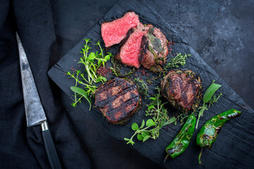 Traditional barbecue dry aged angus medaillon beef filet steak natural with herbs and red wine salt served as top view on a charred wooden board with copy space