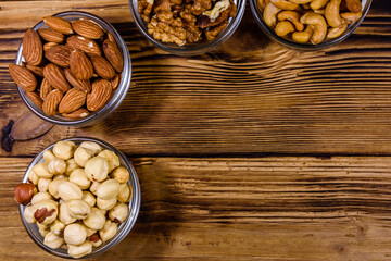 Various nuts (almond, cashew, hazelnut, walnut) in glass bowls on a wooden table. Vegetarian meal. Healthy eating concept. Top view