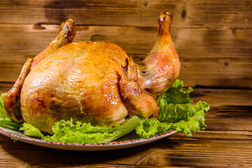 Plate with roasted whole chicken and lettuce leaves on a wooden table