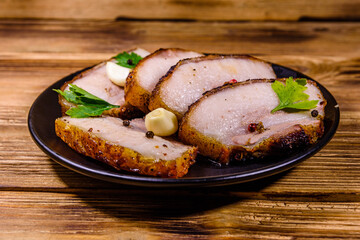 Slices of baked pork belly, garlic and parsley on a black plate