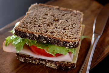 Close up of whole wheat bread slices topped with ham, tomato slice and lettuce leaf.