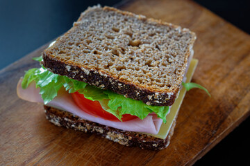 Close up of whole wheat bread slices topped with ham, tomato slice and lettuce leaf.