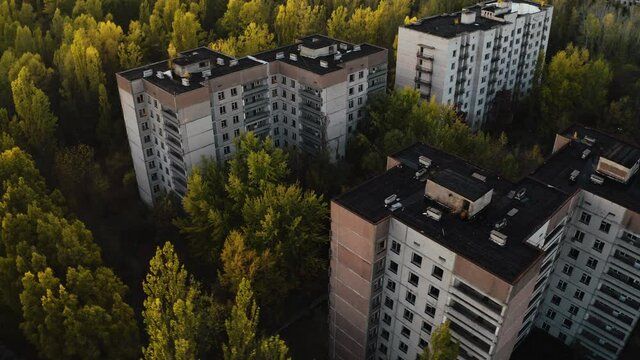 Drone flyover the abandoned city of Pripyat. Destroyed buildings. Overgrown streets of the city. Chernobyl Aerial Drone Video with autumn colors - Sunset evening.