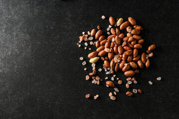 peanuts, dry groundnuts, with Himalayan coarse salt on a dark gray background, top view, empty space for text