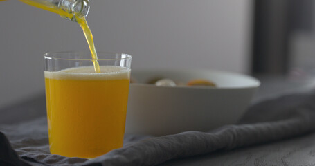man hand pour orange lemonade from glass bottle to tumbler glass on black wood table