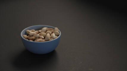 salted large pistachios in blue bowl on black paper background