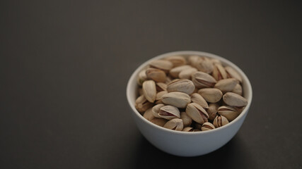 salted large pistachios in white bowl on black paper background