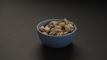 salted large pistachios in blue bowl on black paper background