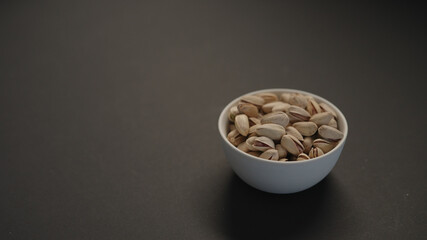 salted large pistachios in white bowl on black paper background