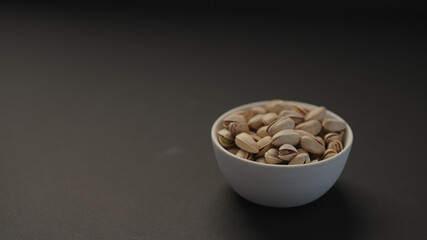 salted large pistachios in white bowl on black paper background