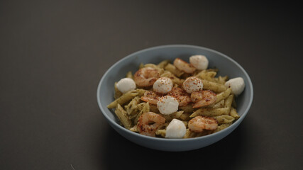 pesto penne with fried shrimps and mozzarella in blue bowl on black background