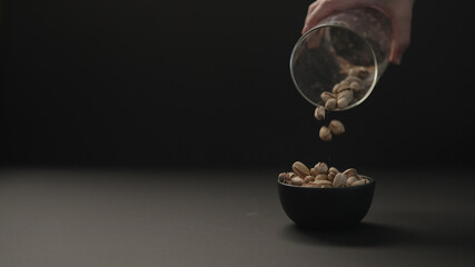 man pour roasted salted pistachios into black bowl on black paper background