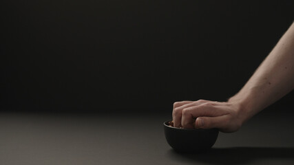 man take roasted hazelnuts from black bowl on black paper background