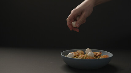 man hand add mozzarella balls to pesto penne with fried shrimps in blue bowl on black background