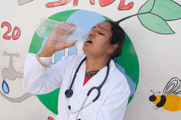 Indian female healthcare professional with a stethoscope around her neck drinking a bottle of water