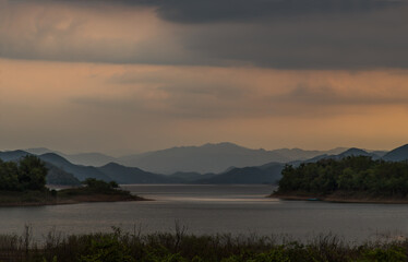 View of lake shore with mountains range in background at sunrise or sunset. Selective focus.