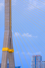 Focus at large pillar and wire ropes of Rama 8 suspension bridge in front of high buildings with blue sky background in Bangkok, Thailand