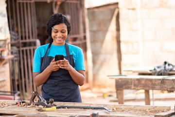 female african worker smiling while using her phone at her workshop