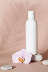Obraz na płótnie Canvas Mock up of white bottle lotion bottle with pink orchid flower, stone and tropical leaf shadow on beige background.Natural organic cosmetics concept