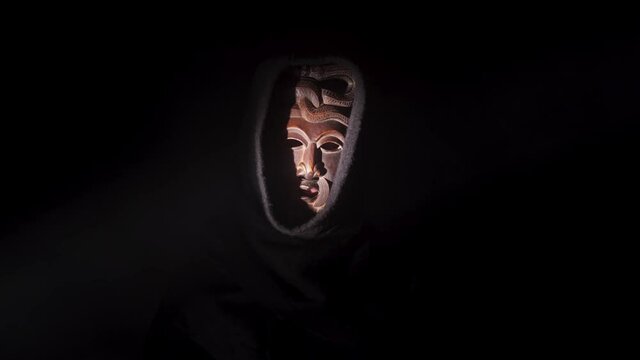 Creepy, masked cultist standing in a dark room. Scary horror scene, mysterious man in a tribal mask isolated on a black background. Eerie mask, devil concept.