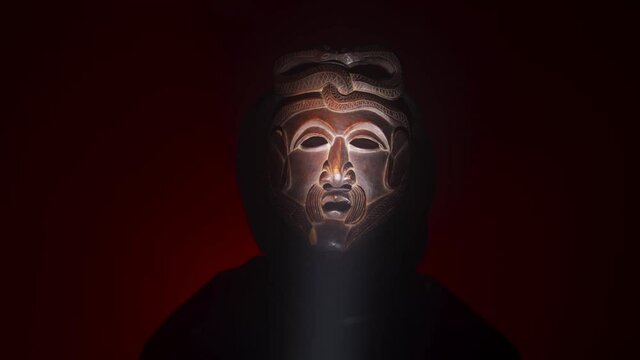 Creepy, masked cultist standing in a dark room. Scary horror scene, mysterious man in a tribal mask isolated on a black background. Eerie mask, devil concept.