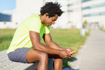 Black man consulting his smartphone with some exercise app while resting from his workout.