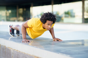 Black man doing triceps dip exercise on city street bench.