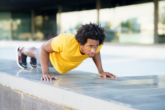 Black man doing triceps dip exercise on city street bench.