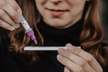 Frau testet sich selbst auf Corona Virus Covid-19 mittels Selbsttest zu Hause und tropft Probe auf...