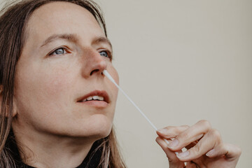 Frau führt Teststäbchen für Covid-19 Selbsttest in die Nase ein um eine Probe zu entnehmen - obrazy, fototapety, plakaty