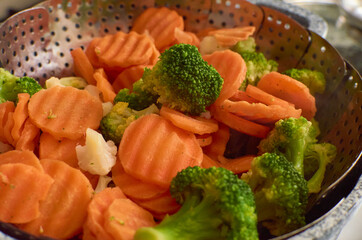 Cooking of steamed sliced vegetables veggies broccoli, cauliflower, carrot medley, mix in steamer basket pot. Healthy eating, lifestyle, bright and colorful food photo.