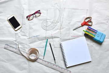 Sewing supplies on a draft paper of pants, sewing thread, scissors, , colorful pen, pencil, ruler, sketch book, smartphone ,centimeter tape and equipment