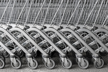Row of supermarket shopping cart trolleys, black and white industrial metal background