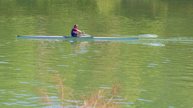 Un uomo concorrente di canottaggio pagaia sul tranquillo fiume da solo