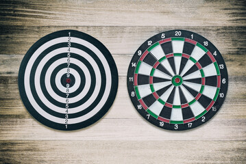 Two styles of dart boards with on brown wooden table on dark tone