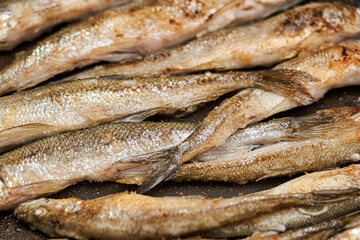 Crispy breaded European smelt fish in a black kitchen pan. Small fish fry in a pan