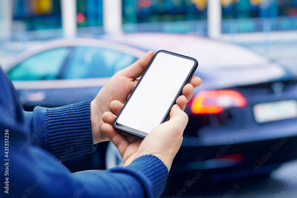 Poster man holds a smartphone in his hands. mock up phone with white screen on the background of the car.