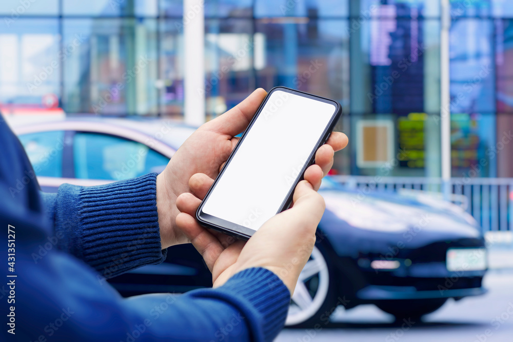 Poster man holds a smartphone in his hands. mock up phone with white screen on the background of the car.