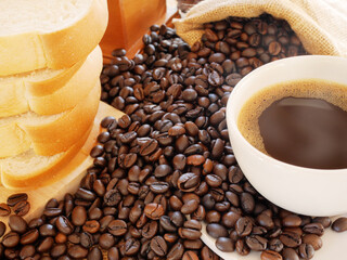 A hot aroma coffee in white cup and sack of coffee beans with bread on the table