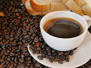 A cup of  hot aroma coffee and a lot of coffee beans with some breads for this breakfast
