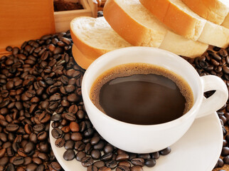 A cup of  hot aroma coffee and more coffee beans with some breads for this breakfast